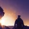 Silhouette of a hiker climbing up a mountain trail at sunrise with sun flares and mountains in the background.